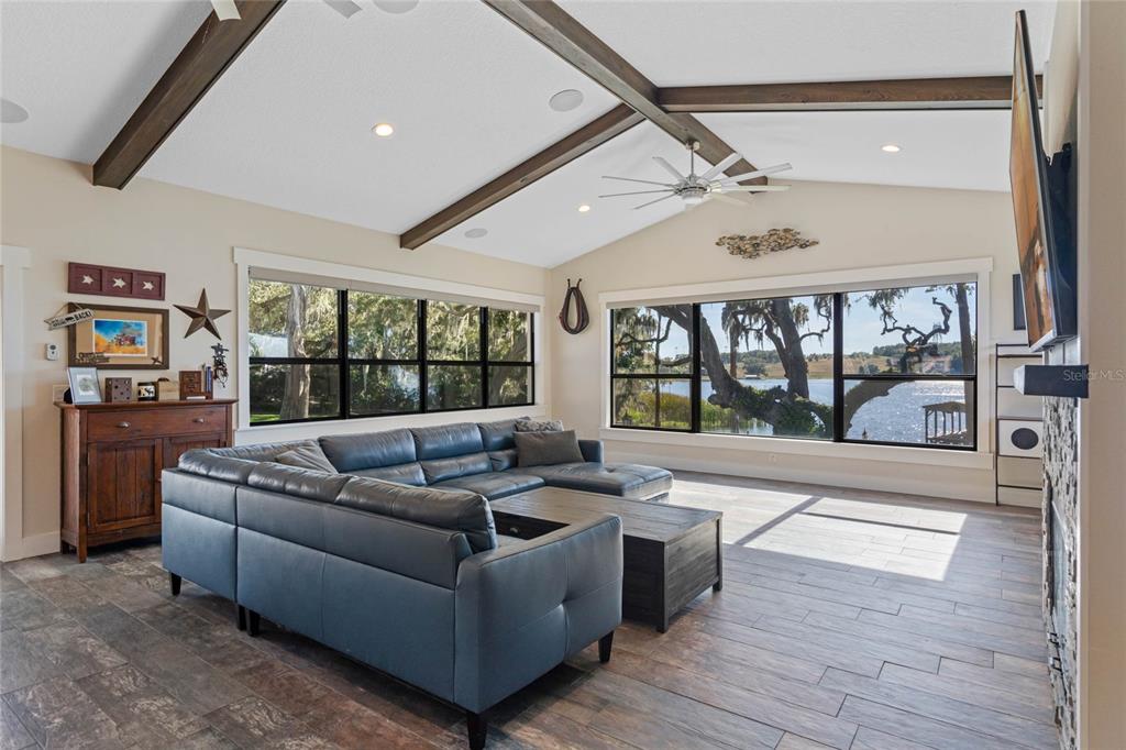 A living room features a blue sectional sofa, vaulted ceilings with exposed beams, and lake views — 17531 COUNTY ROAD 455, MONTVERDE, FL