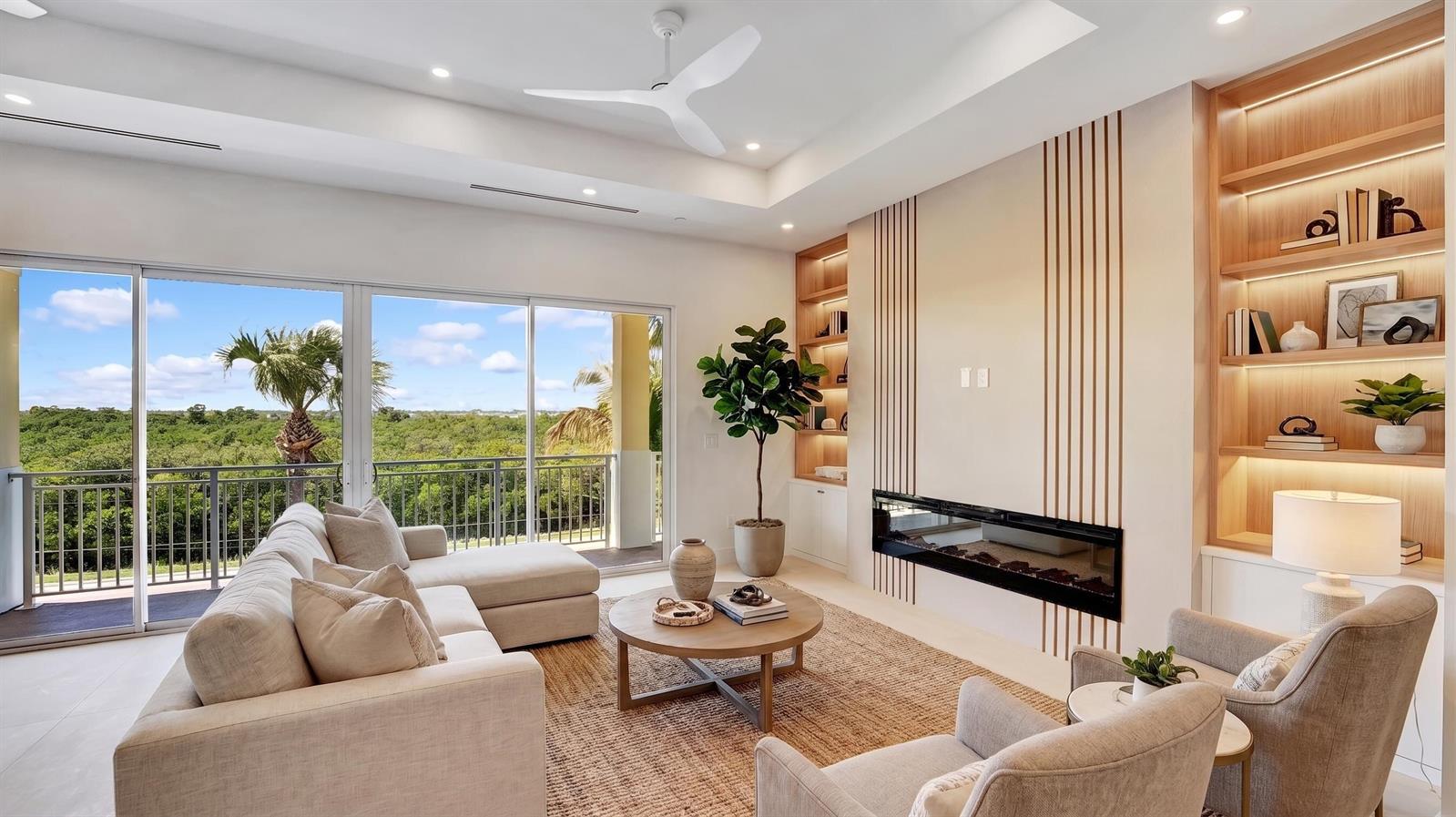 A modern living room features a fireplace, built-in shelving, a sectional sofa, and balcony views — 4857 Watersong Way, Fort Pierce FL 34949, FORT PIERCE, FL