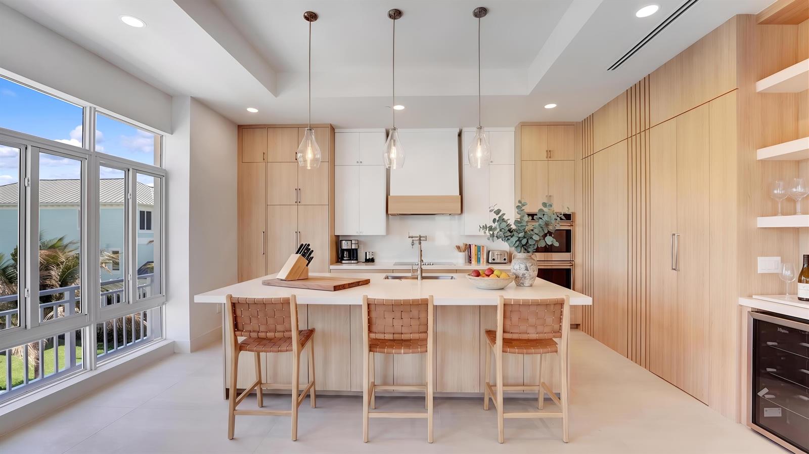 A modern kitchen features a central island with three woven stools and light wood cabinetry — 4857 Watersong Way, Fort Pierce FL 34949, FORT PIERCE, FL