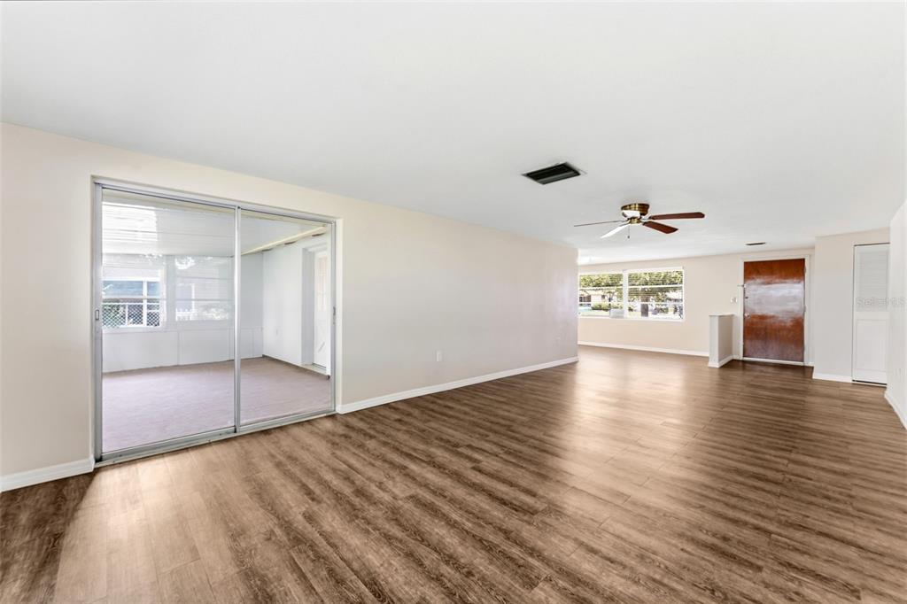 A spacious living room features wood-look flooring, a ceiling fan, and sliding glass patio doors — 7814 TALISMAN DRIVE, PORT RICHEY, FL