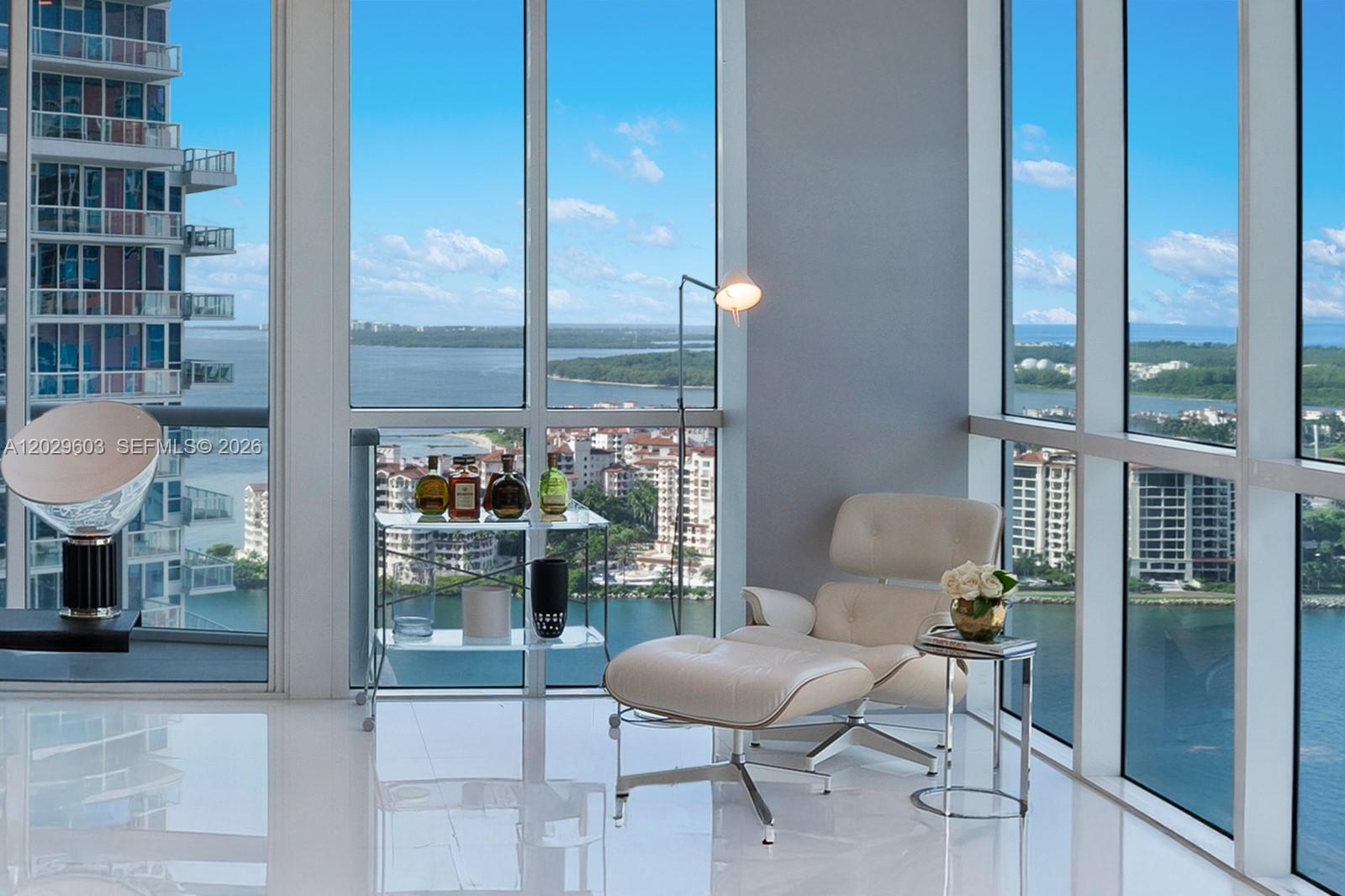A modern room with floor-to-ceiling windows, a lounge chair, and a bar cart overlooking water — 50 S Pointe Dr # 2903, Miami Beach FL 33139, MIAMI BEACH, FL