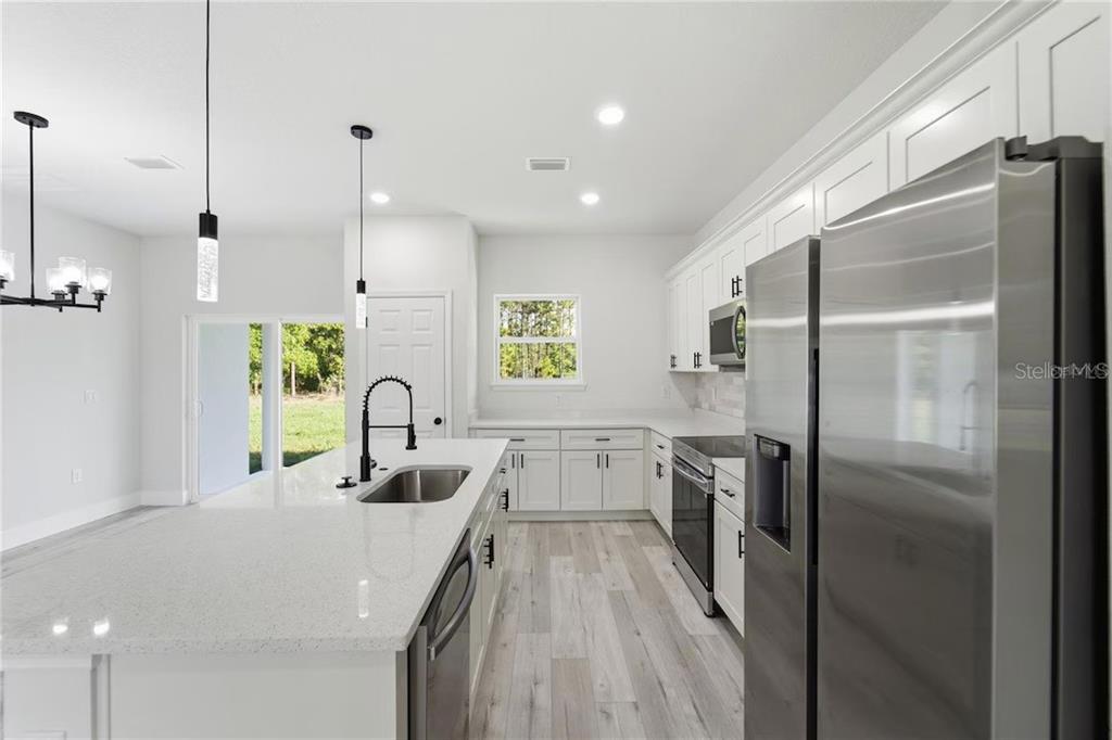 A modern kitchen features white cabinets, stainless steel appliances, a quartz island, and wood-look flooring — 3286 W CRANDON DRIVE, CITRUS SPRINGS, FL