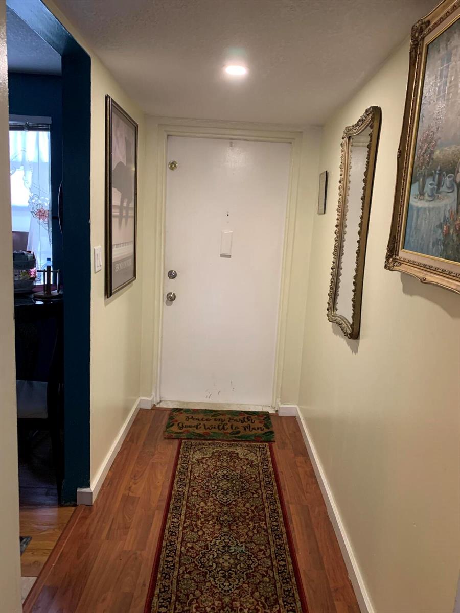 A hallway with wood flooring, a white front door, a runner rug, and wall art — 7887 Golf Cir Drive # 212, Margate FL 33063, MARGATE, FL