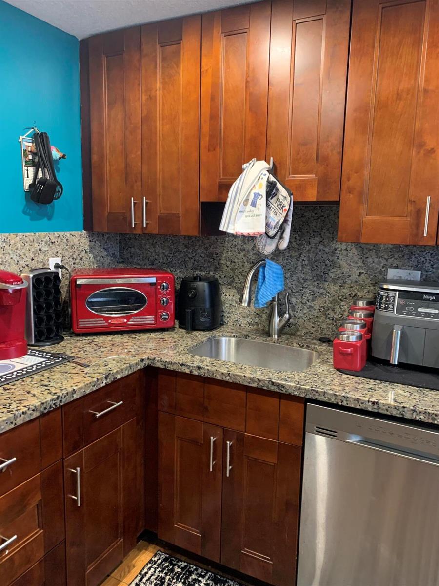 A kitchen features wood cabinets, granite countertops, a stainless steel sink, and various small appliances — 7887 Golf Cir Drive # 212, Margate FL 33063, MARGATE, FL