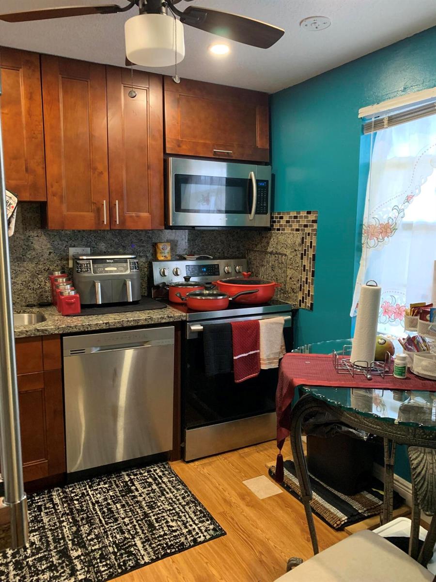 A kitchen features wood cabinets, stainless steel appliances, granite countertops, and a teal accent wall — 7887 Golf Cir Drive # 212, Margate FL 33063, MARGATE, FL