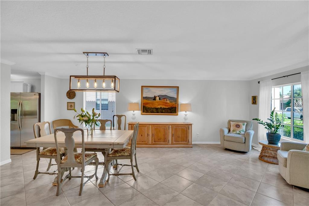 A dining room with a wooden table, chandelier, sideboard, and two armchairs on tiled floors — VERO BEACH, FL
