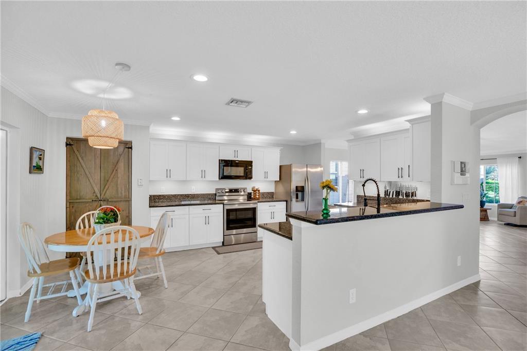 A kitchen with white cabinets, dark granite countertops, stainless steel appliances, and a dining area — VERO BEACH, FL