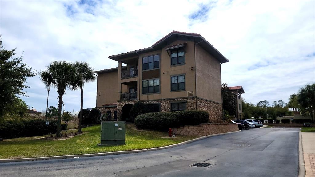 A three-story apartment building with stucco and stone siding sits next to a paved road — 914 CHARO PARKWAY UNIT 123, DAVENPORT, FL