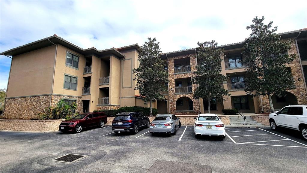 A multi-story apartment building with stone and stucco siding sits behind a paved parking lot — 914 CHARO PARKWAY UNIT 123, DAVENPORT, FL