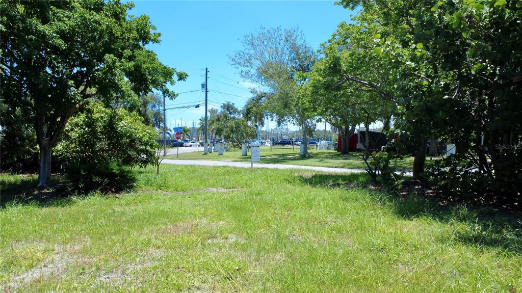 A grassy, tree-lined vacant lot features a paved road and a distant marina in view — 4725 TRADE WINDS DRIVE S, GULFPORT, FL