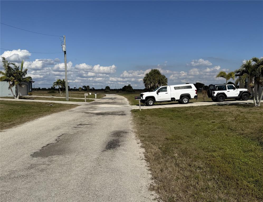 A paved road leads past two houses with driveways and parked vehicles under a blue sky — 8 LAUREL COURT, PLACIDA, FL