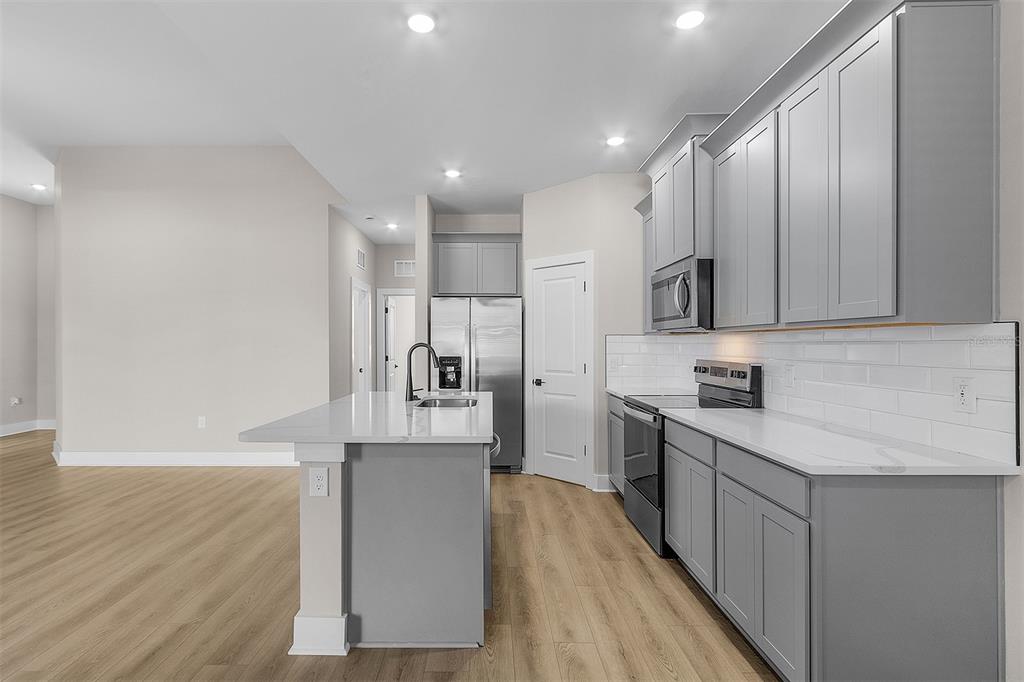 A modern kitchen features gray cabinets, white countertops, a center island, and light wood flooring — 2405 GALLAGHER ROAD, DOVER, FL