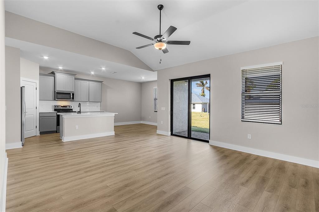 An open-concept living area features light wood-look flooring, a kitchen with gray cabinets, and sliding doors — 2405 GALLAGHER ROAD, DOVER, FL