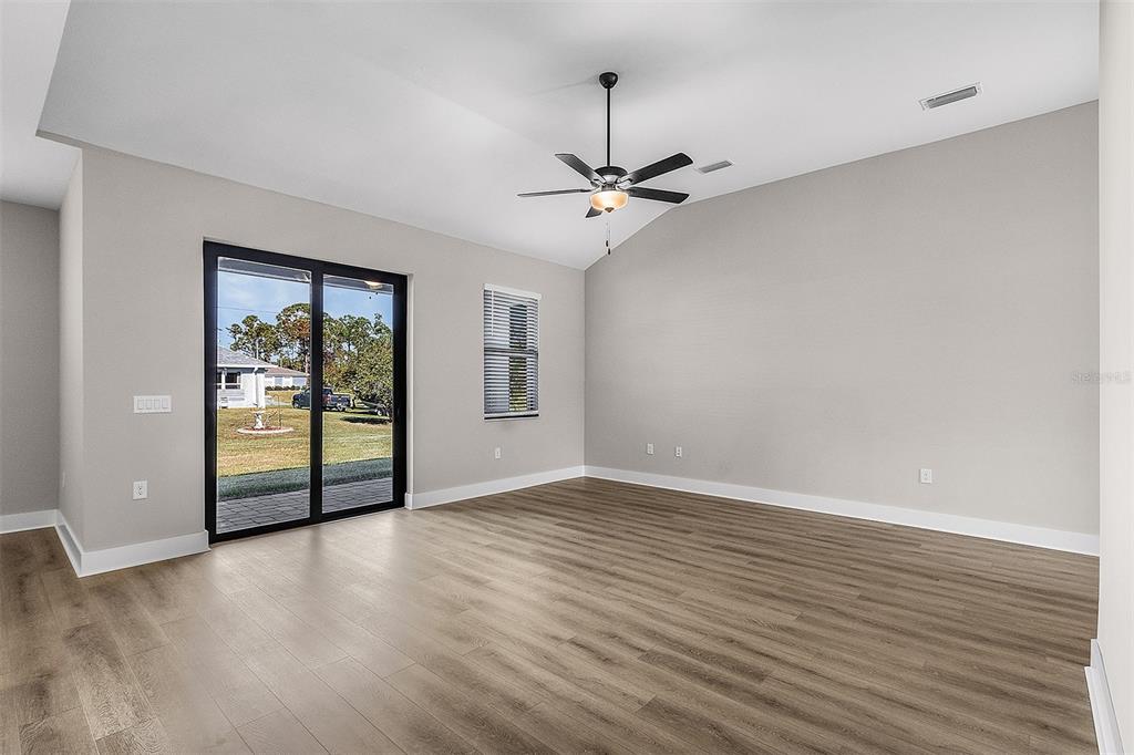 An empty living room with light gray walls, wood-look flooring, a ceiling fan, and sliding doors — 2405 GALLAGHER ROAD, DOVER, FL