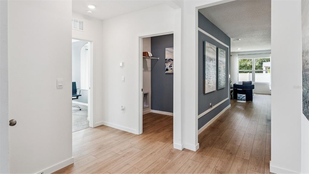 A hallway with light wood-look flooring leads to a blue-accented living area and office — 805 MASSY COURT, KISSIMMEE, FL