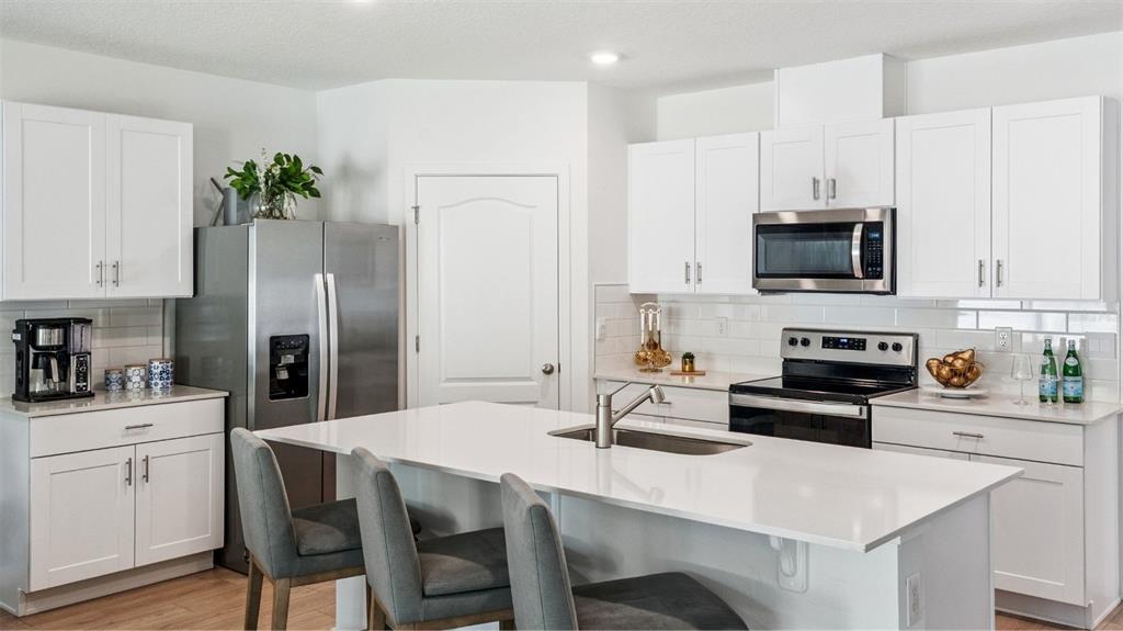 A modern kitchen features white cabinets, stainless steel appliances, and a central island with seating — 805 MASSY COURT, KISSIMMEE, FL