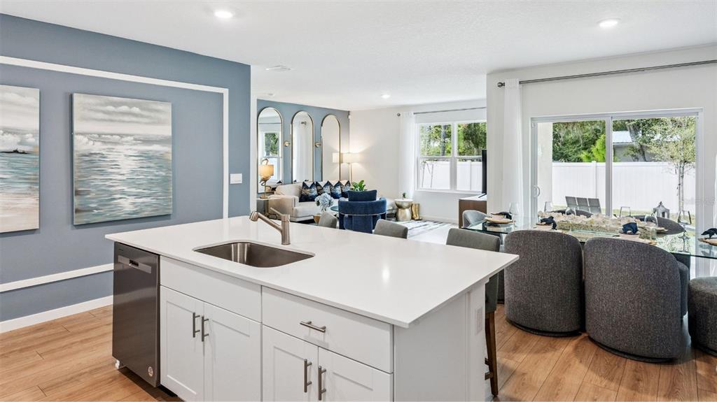 A kitchen island with a white countertop and sink overlooks an open-concept living and dining area — 805 MASSY COURT, KISSIMMEE, FL