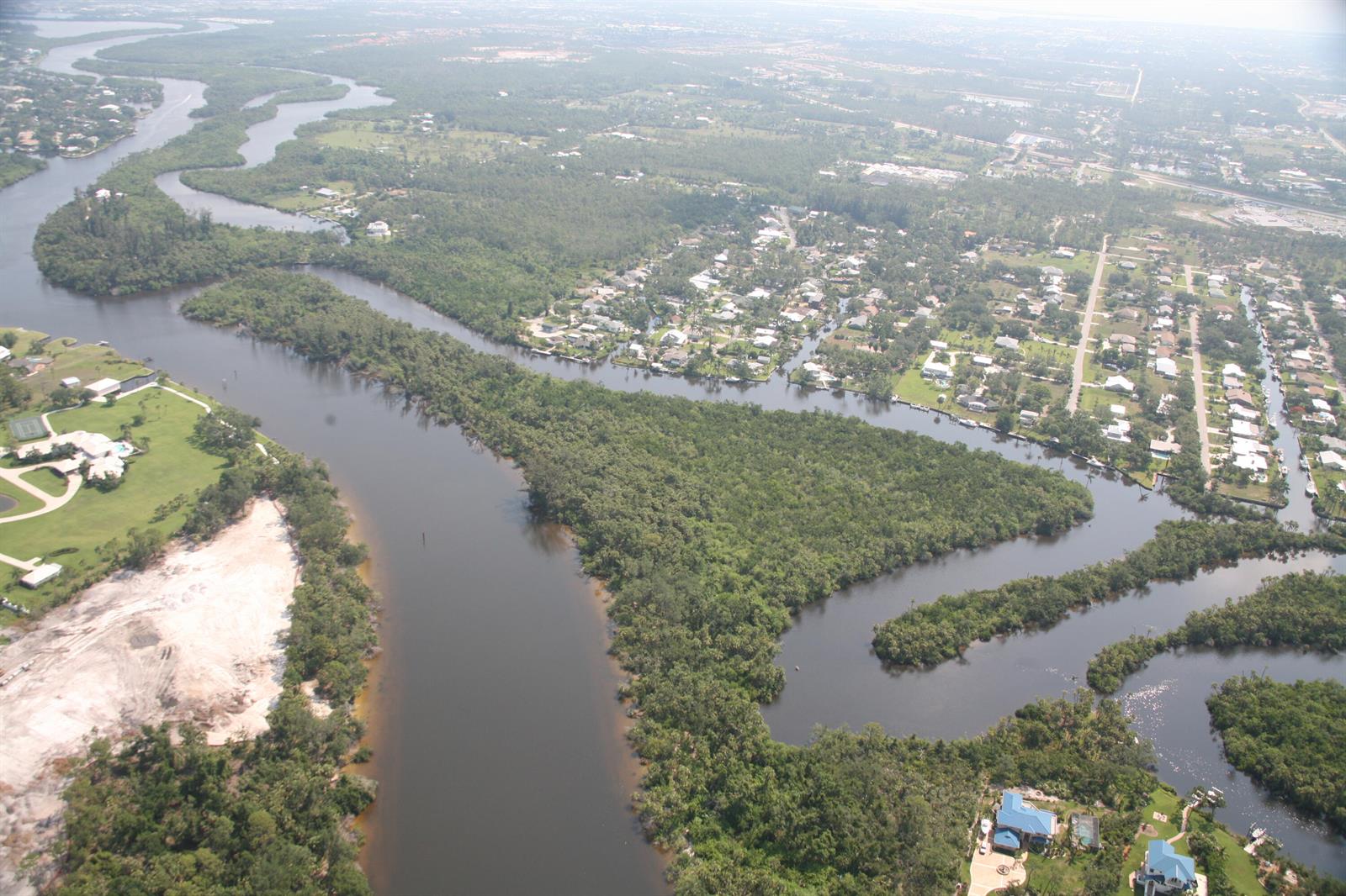 An aerial view shows a winding river flowing through a residential area with dense vegetation — 0 Blue Water Way, Stuart FL 34997, STUART, FL