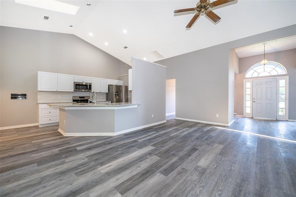 A bright, open-concept living area features gray wood-look flooring, a vaulted ceiling, and a kitchen — 7304 HIGH LAKE DRIVE, ORLANDO, FL