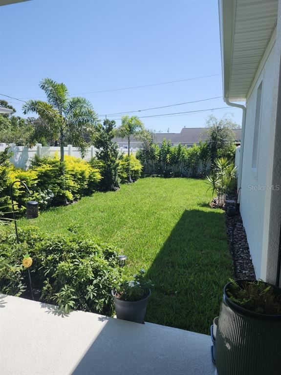 A view of a grassy backyard with a patio, landscaping, and a white privacy fence — 4810 EMERSON AVENUE S, ST PETERSBURG, FL