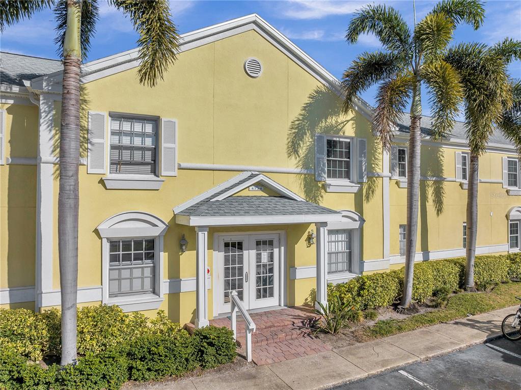 A yellow two-story building with a covered entrance and palm trees in front — 4728 BEACH DRIVE SE UNIT A, ST PETERSBURG, FL