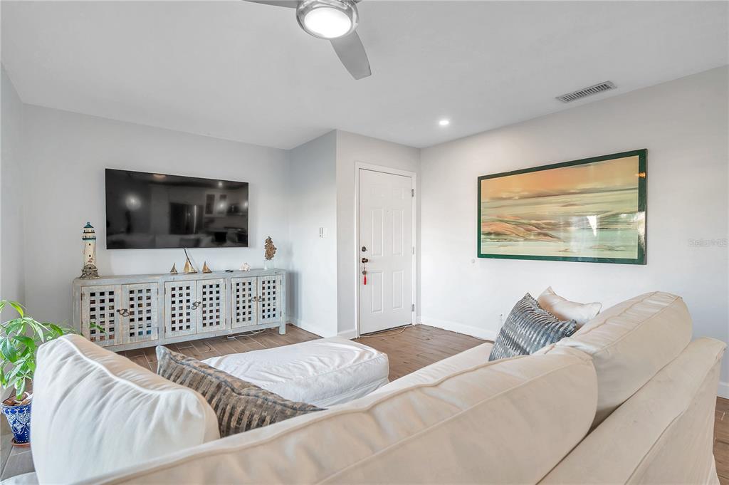 A living room with light wood-look flooring, a white sofa, and an open-concept kitchen — 4728 BEACH DRIVE SE UNIT A, ST PETERSBURG, FL
