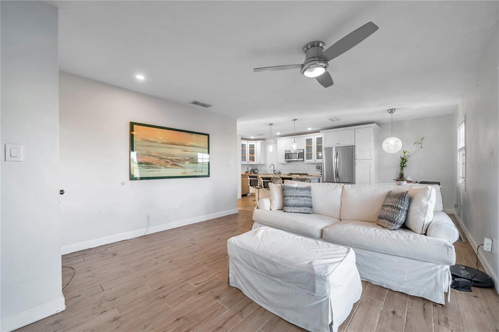 A living room features a white sofa, a light-colored media console, and a wall-mounted television — 4728 BEACH DRIVE SE UNIT A, ST PETERSBURG, FL
