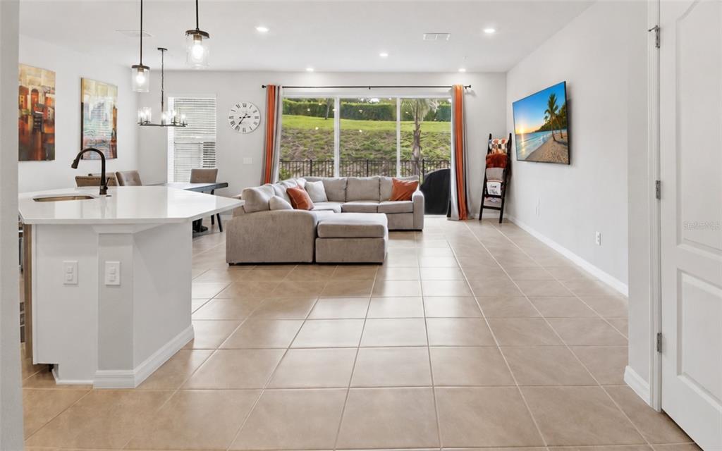 An open-concept living room and kitchen area features tile flooring, a sectional sofa, and windows — 547 ASTERA WINDS LANE, LAKE MARY, FL