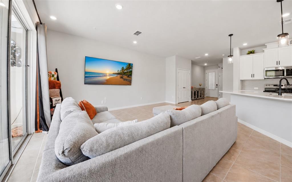 A living room with a gray sectional sofa faces a wall-mounted television near a kitchen — 547 ASTERA WINDS LANE, LAKE MARY, FL