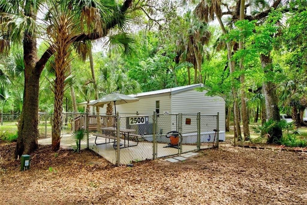 A mobile home with a fenced-in patio and picnic table sits in a wooded area — 2500 ARBUCKLE SHORES ROAD, FROSTPROOF, FL