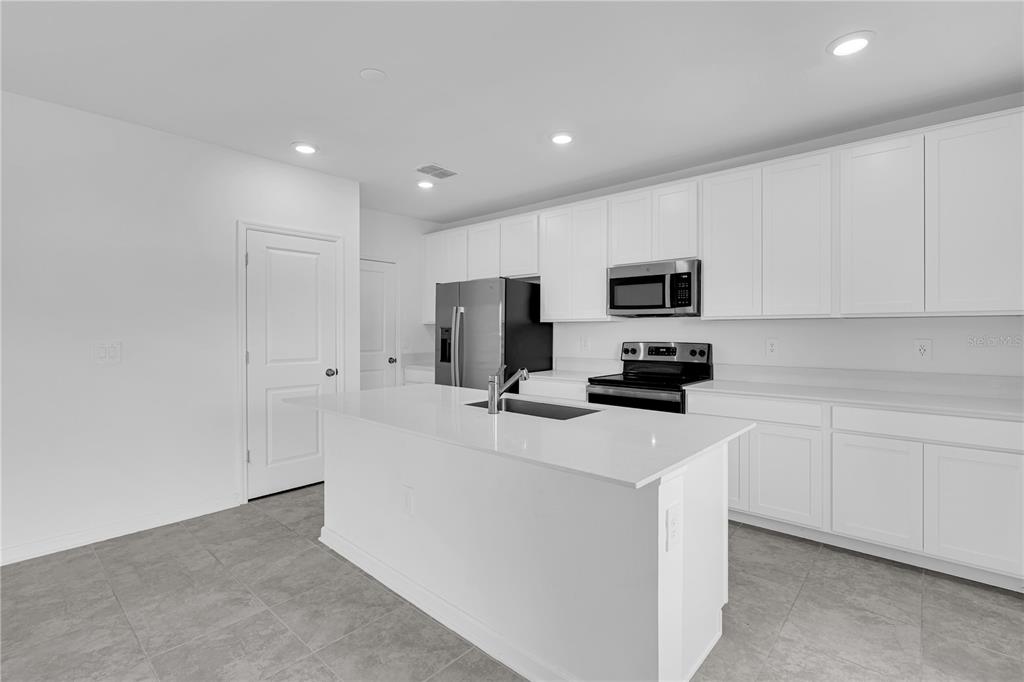 A modern kitchen features white cabinets, a central island with a sink, and stainless appliances — 1021 WATERFALL BOULEVARD, DAVENPORT, FL