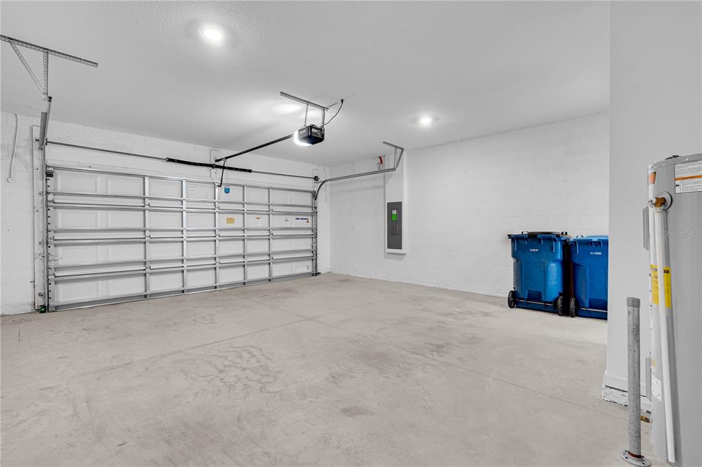 An empty garage features a white sectional door, concrete floors, and a water heater — 1021 WATERFALL BOULEVARD, DAVENPORT, FL