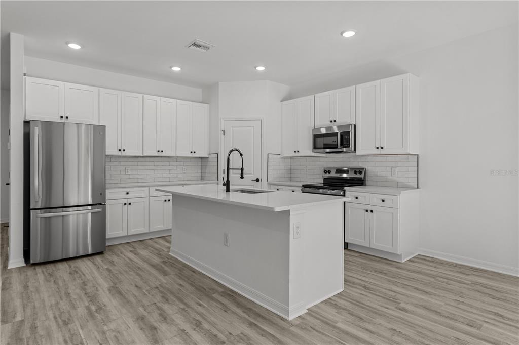 A modern kitchen features white cabinets, stainless steel appliances, a center island, and wood-look flooring — 12232-12234 NEWGATE AVENUE, PORT CHARLOTTE, FL