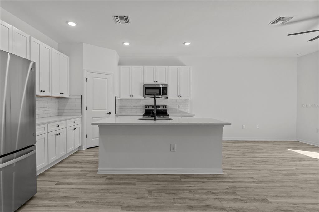 A modern kitchen features white cabinets, stainless steel appliances, a center island, and wood-look flooring — 12232-12234 NEWGATE AVENUE, PORT CHARLOTTE, FL