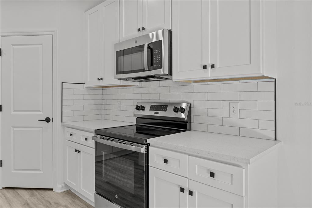 A kitchen features white cabinets, stainless steel appliances, and a white subway tile backsplash — 12232-12234 NEWGATE AVENUE, PORT CHARLOTTE, FL