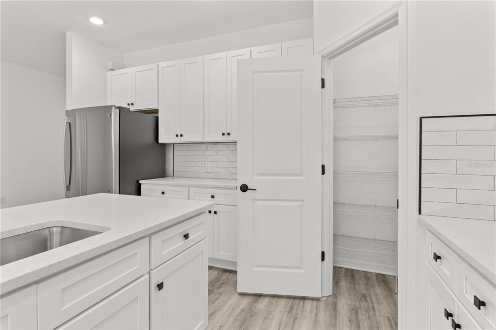 A kitchen features white cabinets, quartz countertops, stainless steel appliances, and an open pantry door — 12232-12234 NEWGATE AVENUE, PORT CHARLOTTE, FL