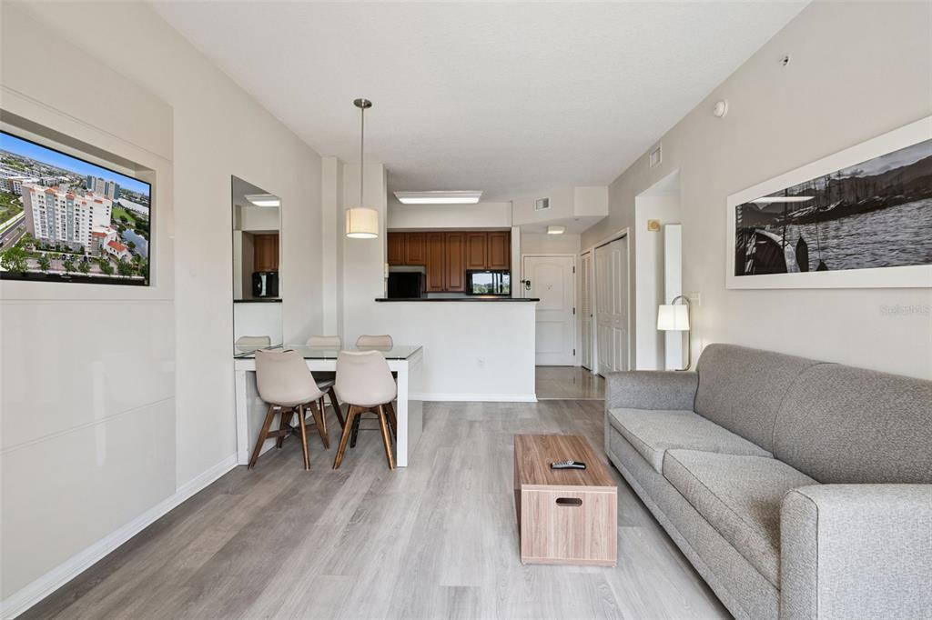 A living room and dining area with light wood floors, a grey sofa, and kitchen — 7395 UNIVERSAL BOULEVARD UNIT 403, ORLANDO, FL