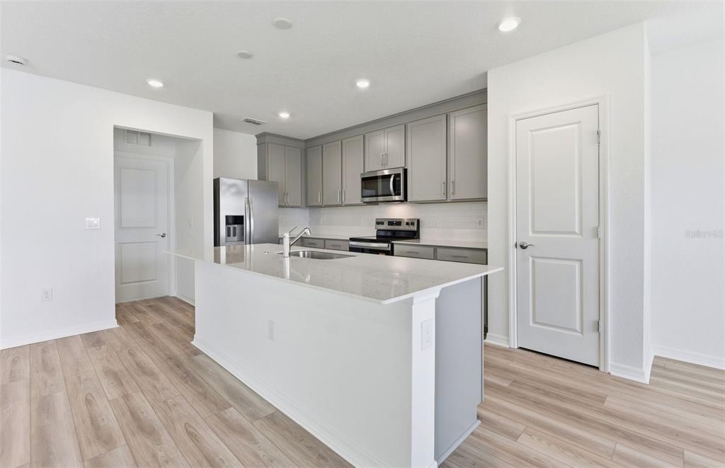 A modern kitchen features gray cabinetry, a white quartz island, and light wood-look flooring — 1448 HAMILTON WAY, LAKE ALFRED, FL