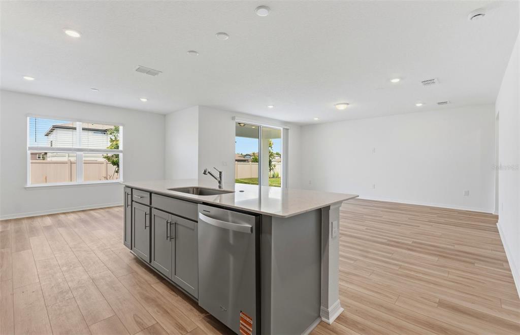 A kitchen island with a stainless steel dishwasher and sink sits in an open-concept room — 1448 HAMILTON WAY, LAKE ALFRED, FL