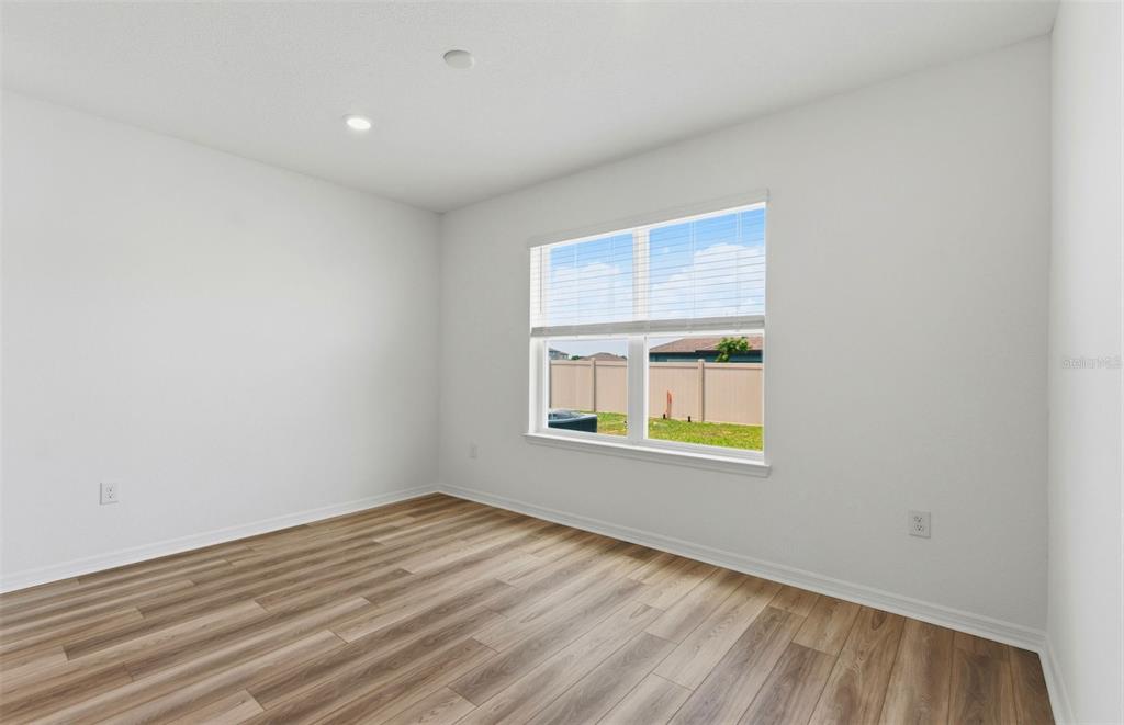 An empty bedroom features white walls, wood-look flooring, and a window overlooking a fenced yard — 1448 HAMILTON WAY, LAKE ALFRED, FL