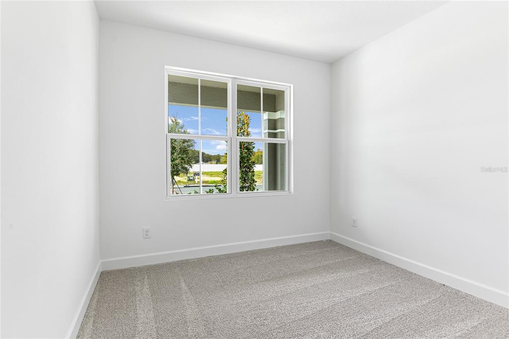 A small, empty bedroom with white walls, gray carpet, and a window overlooking construction — 178 BLUE STAR COURT, TAVARES, FL