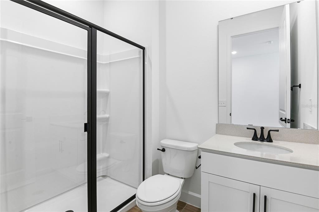 A bathroom features a glass-enclosed shower, a white vanity, and a toilet against white walls — 178 BLUE STAR COURT, TAVARES, FL