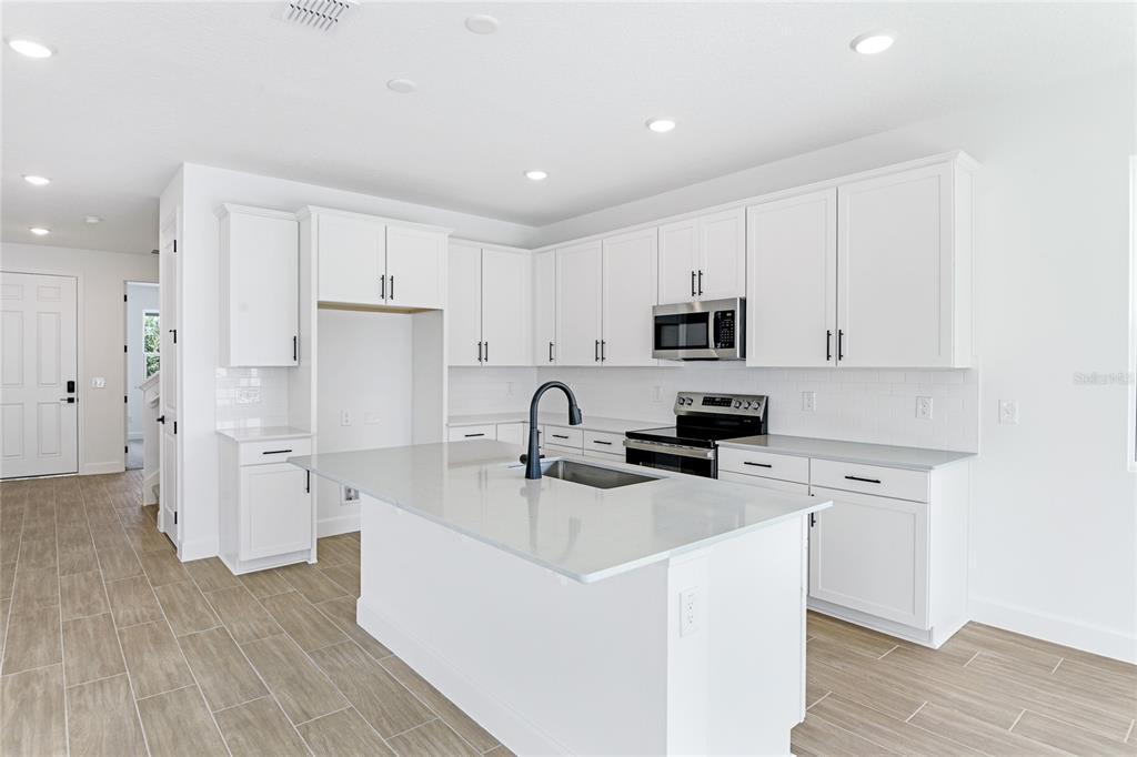 A modern kitchen features white cabinets, a large island with a sink, and tile flooring — 178 BLUE STAR COURT, TAVARES, FL