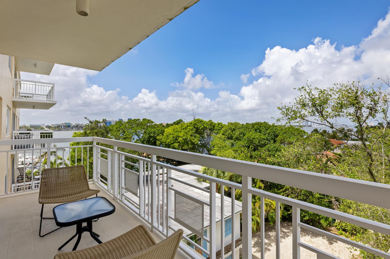 A balcony with two chairs and a small table overlooks trees and a distant waterway — 250 Bradley Place # 606, Palm Beach FL 33480, PALM BEACH, FL