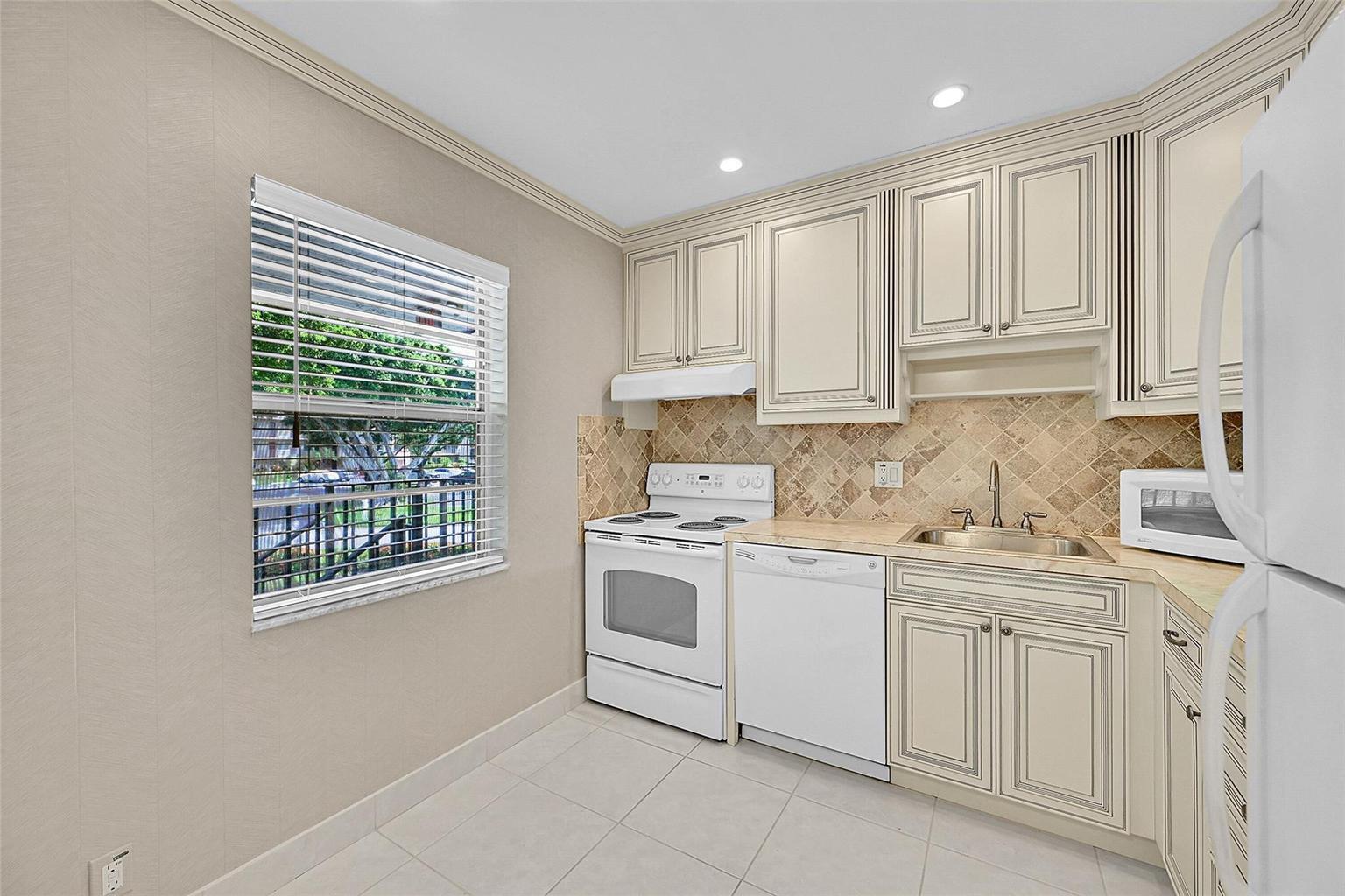 A kitchen features cream-colored cabinets, white appliances, a tiled backsplash, and a window — 23 Abbey Lane # 202, Delray Beach FL 33446, DELRAY BEACH, FL