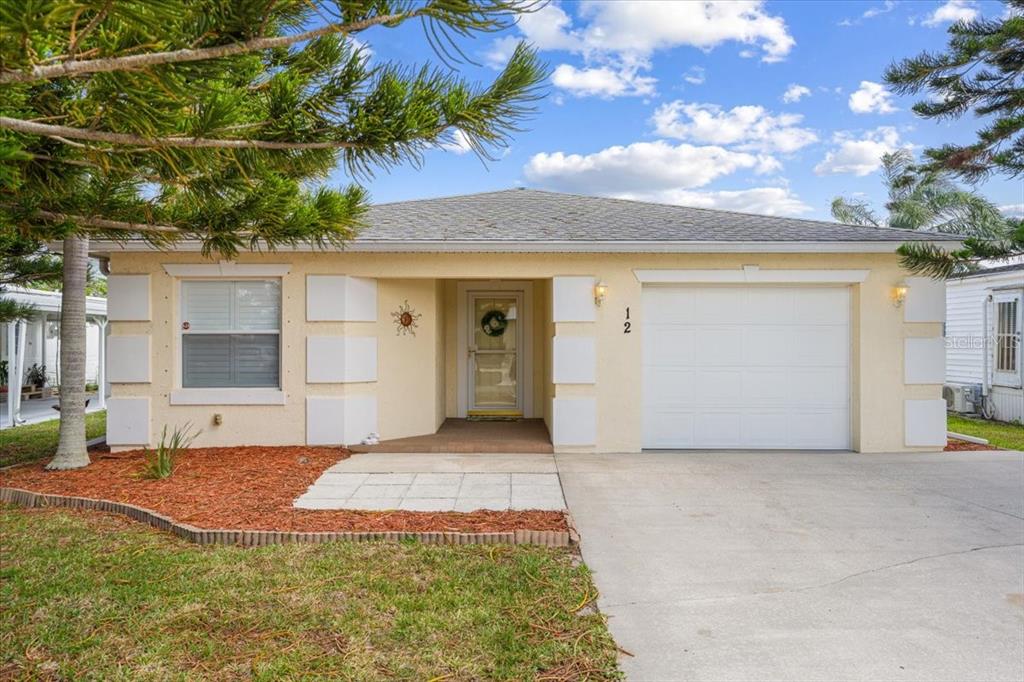 A single-story house with a light yellow stucco exterior, a white garage door, and a driveway — 12 PALO ALTO LANE, PORT ST LUCIE, FL