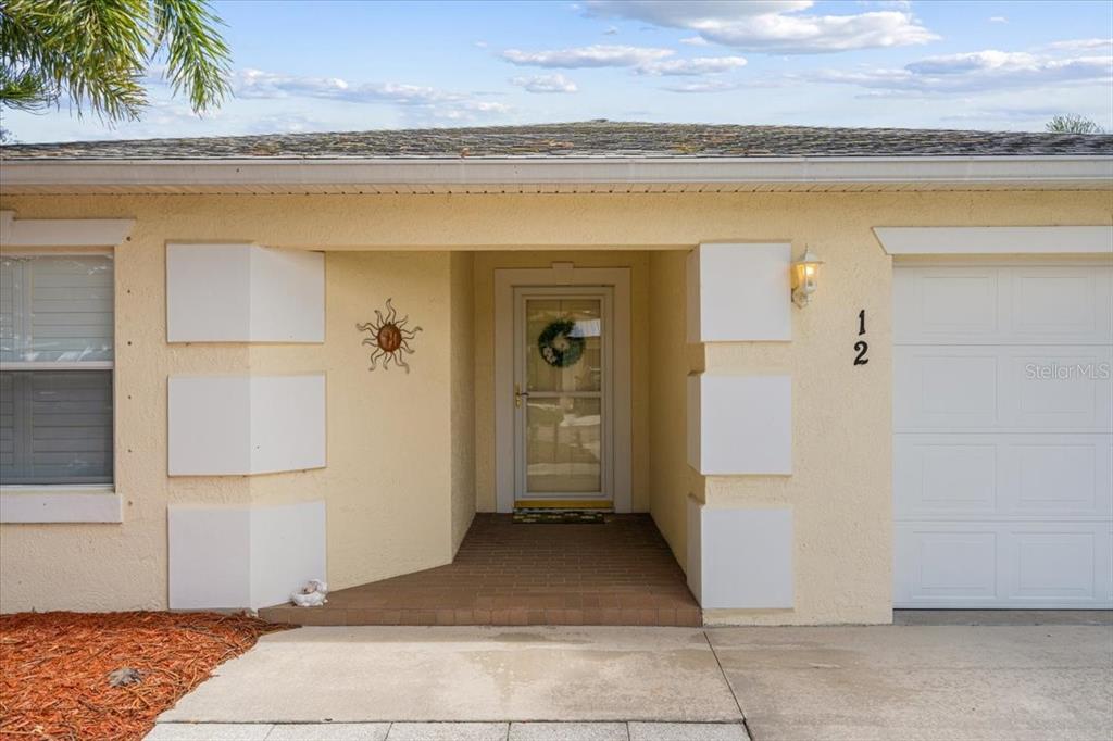 The exterior of a house features a tan stucco facade, a brick entryway, and a garage — 12 PALO ALTO LANE, PORT ST LUCIE, FL