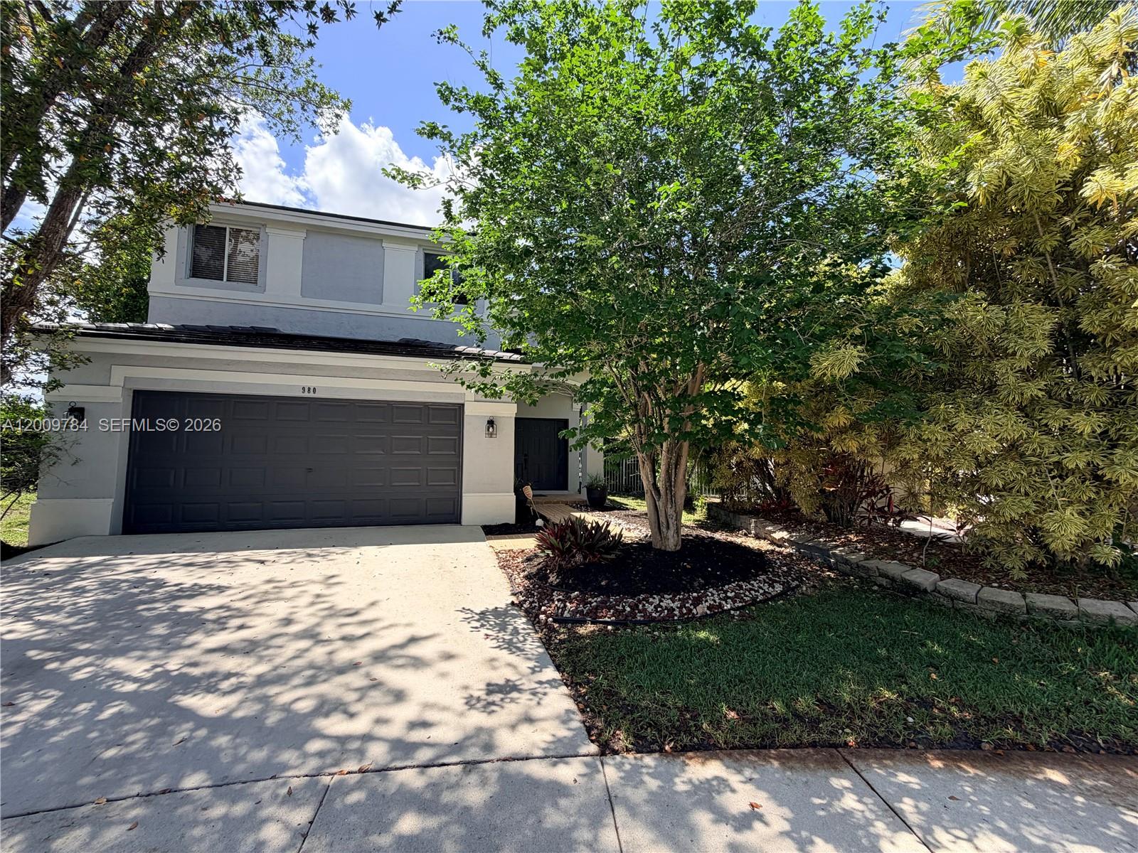 A two-story house features a gray garage, a paved driveway, and a large front tree — 980 Golden Cane Dr, Weston FL 33327, WESTON, FL