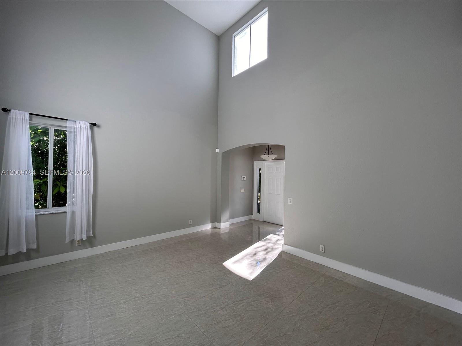 An empty living room with high ceilings, tile floors, and a view of the entryway — 980 Golden Cane Dr, Weston FL 33327, WESTON, FL