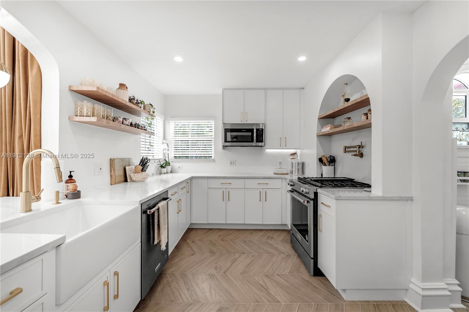 A white kitchen features wood-look herringbone floors, open shelving, and an arched stove alcove — 1601 Washington St, Hollywood FL 33020, HOLLYWOOD, FL